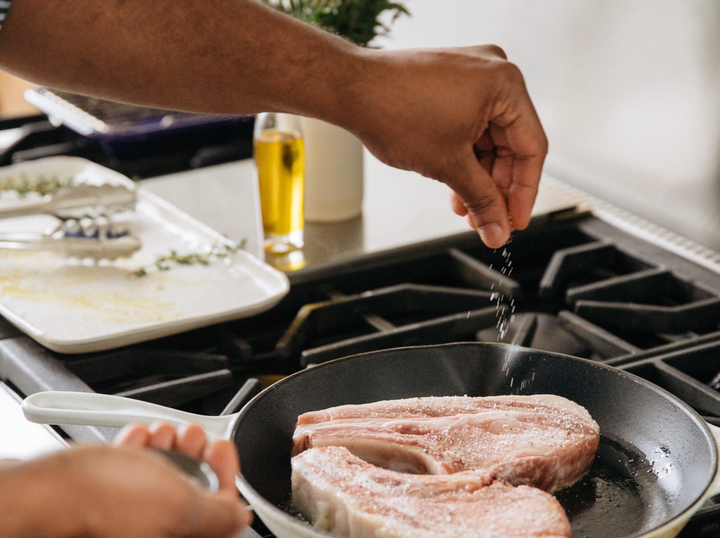 Adding salt to pork chops on a frying pan