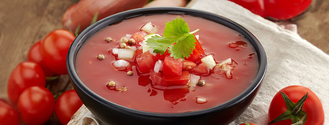gazpacho in a bowl with tomatoes around the bowl